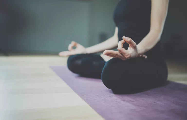 Mulher vestida de preto fazendo meditação em tapete: pernas cruzadas em posição de lótus
