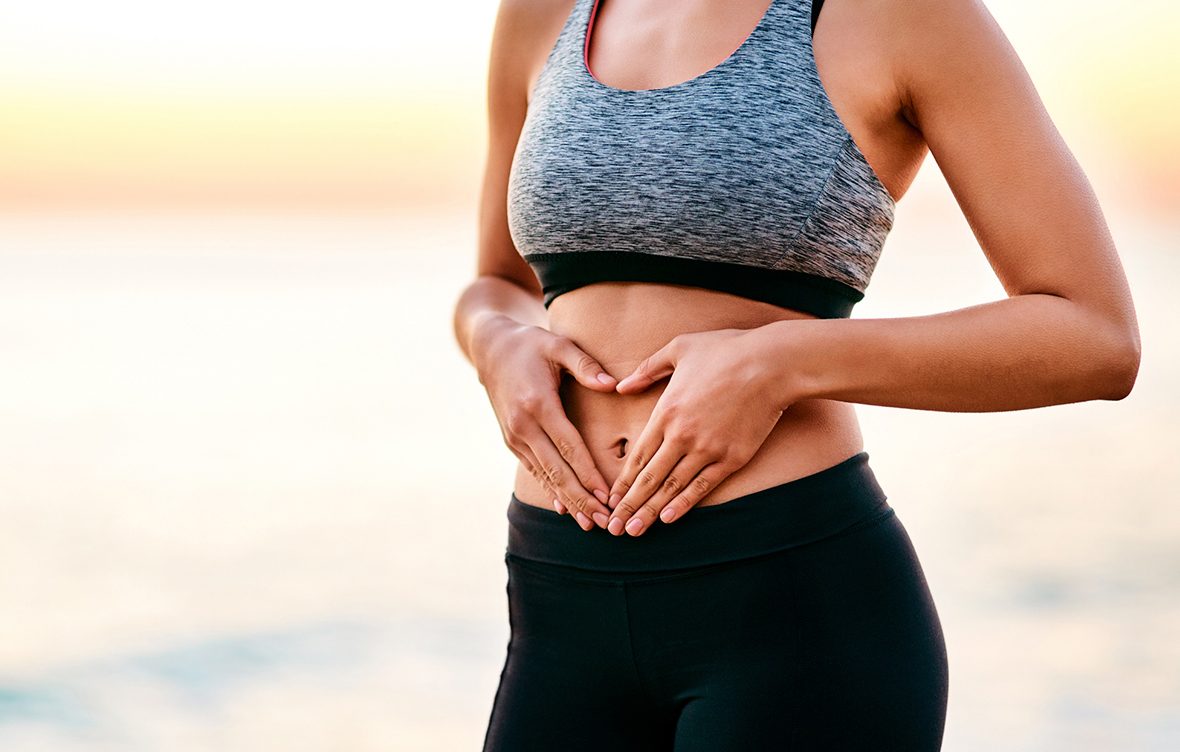 Mulher com roupa de malhar com mãos em cima da barriga sarada com o umbigo entre os dedos